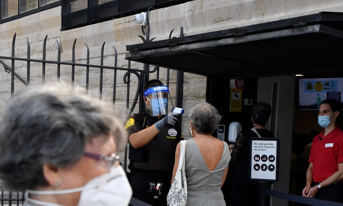 People wearing face masks queue while a security guard uses a thermometer to check the temperature of a woman before attending a mass for victims of the COVID-19 coronavirus at the Sagrada Familia in Barcelona.