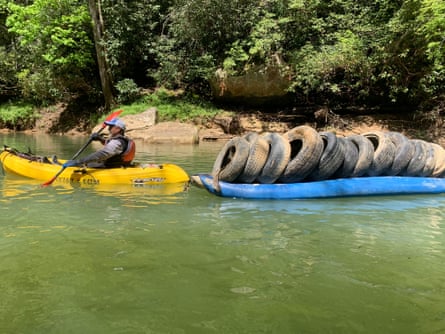 a man on a boat drags another boat filled with over a dozen tires on it