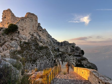 Soldiers walk along a path on the cliff beside the castle, beneath a bright blue sky