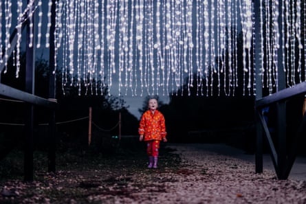 A child in a red raincoat looks up at hundreds of hanging string lights at twylight