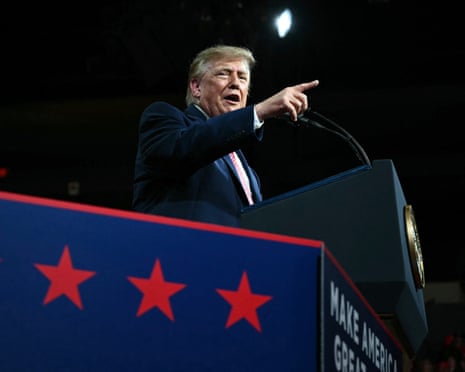 Donald Trump at a podium with microphones points into the distance while speaking
