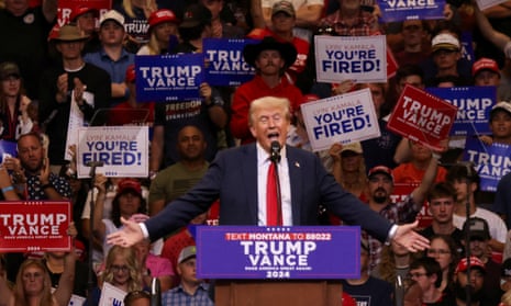 man who is Donald Trump wearing blue suit and red tie stands behind podium and waves hand with crowd of people behind him