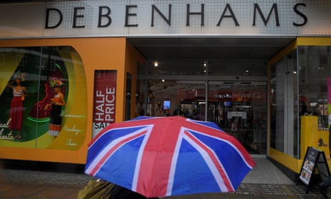 A shopper walks past a Debenhams store in central London clutching a union flag umbrella