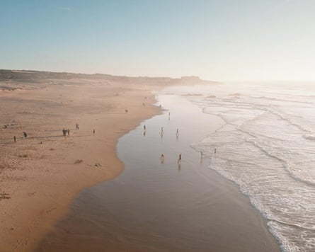 wide open sandy beach coastline at sunset, people relaxing on sand