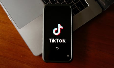 TikTok logo seen on a smartphone resting on a laptop