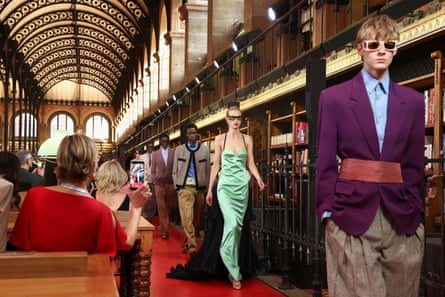 Five models walk down the catwalk in a line dressed in the collection’s designs as spectators seated in pews hold up phones