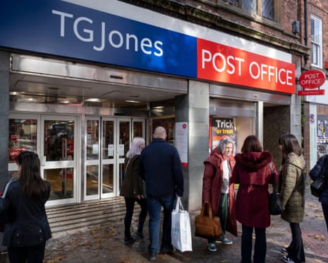 People queue outside a TG Jones Post Office storefront on a high street