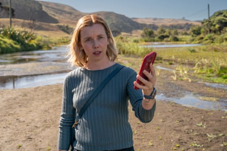 Mia (Lauren Lyle) standing with a phone in her hand in a still from The Ridge