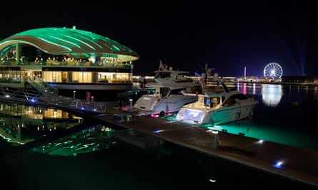 Luxury motorboats parked next to the luxury restaurant Beefbar Qatar at the Lusail Esplanade with the ferris wheel of Winter Wonderland on Al Maha Island in the background.
