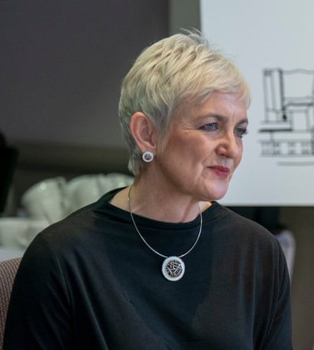 she has short blond hair and wears a black top, a metallic circular pendant necklace with matching earrings, and red lipstick