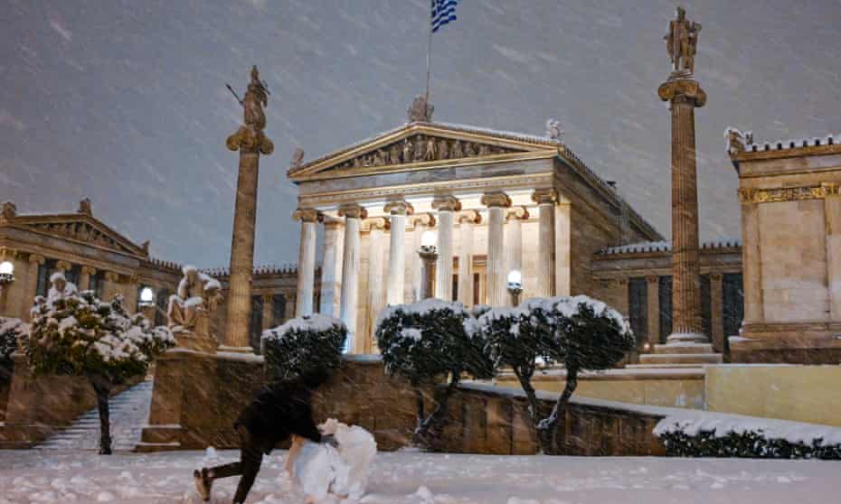 A man makes a snowman in front of Academia during snowstorm in Athens
