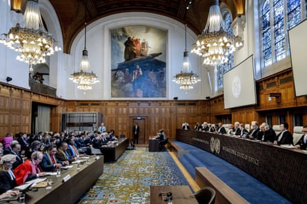 two long desks facing each other, with groups seated behind each one, in a large room with chandeliers and a painting