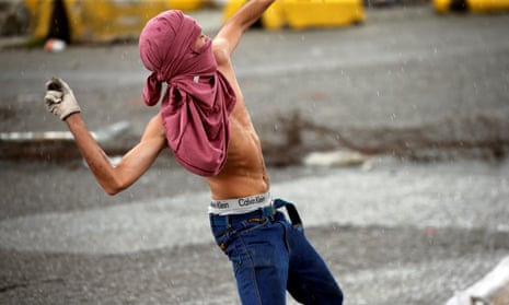 A protester throws rocks during clashes with Venezuelan security forces near a military base, which was attacked by rebels on Sunday. 
