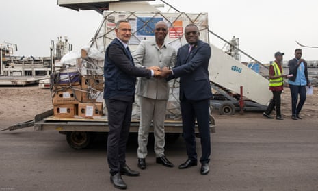 Three men shake hands in front of a loading pallet piled with boxes.