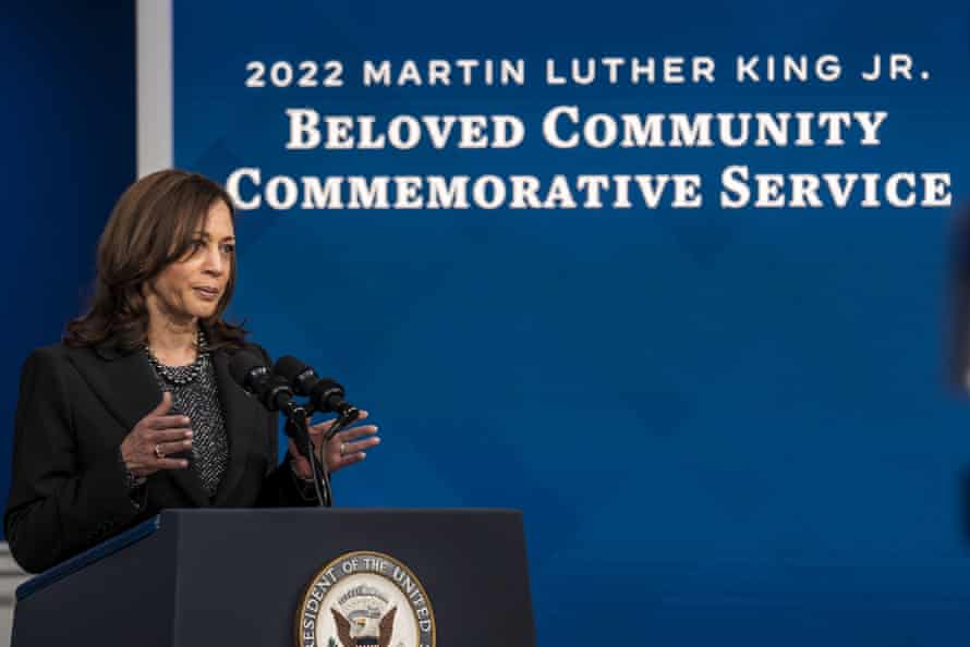 Una donna sta davanti a uno schermo su un palco e dichiara "2022 Martin Luther King Jr. Servizio commemorativo della comunità amorevole".