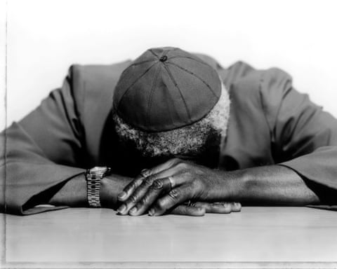 Bishop Desmond Tutu rests his head on the table, hands clasped in front of him