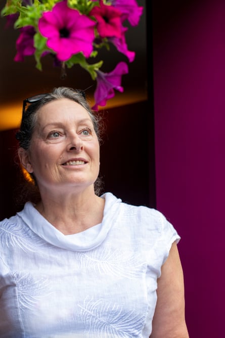 Close up of Kathryn Faulke in a doorway at home in Norfolk wearing a white top - with fuchsia flowers hanging above her head
