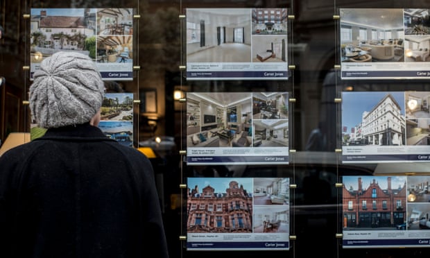 A woman looking at houses for sale in the window of an estate agents in London.