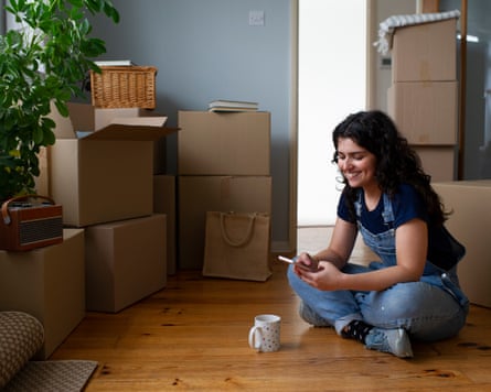 A woman in the middle of a house move, using a smart phone and taking a break