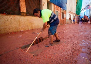 A worker cleans a street covered in tomatoes after La Tomatina in Spain