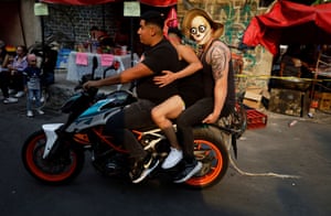 A person wearing a novelty mask rides pillion on the motorcycle