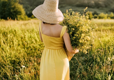 woman in yellow sundress gathering flowers in a field, wearing a big sun hat