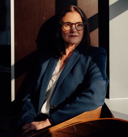 Jennifer Blagg sitting in her office, wearing a petrol-blue blazer with a cream blouse underneath, and glasses, looking at the camera