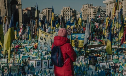 A woman stands in front of a large memorial to killed soldiers and civilians, including many Ukrainian flags and portraits, in the centre of Kyiv.