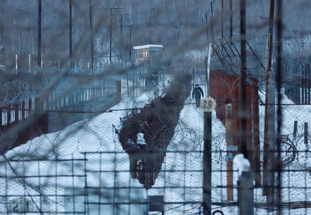 A man walks through snow between barbed wire fences