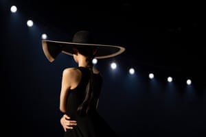 A model on the catwalk, wearing a wide brimmed hat, with dramatic spot lighting