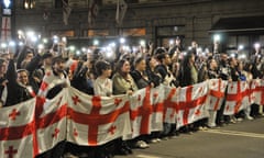 A line of protesters hold Georgian flags as others behind them hold up phones