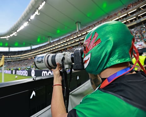 A photographer dons a Mexican wrestling mask during Mexico v South Korea in Guadalajara.