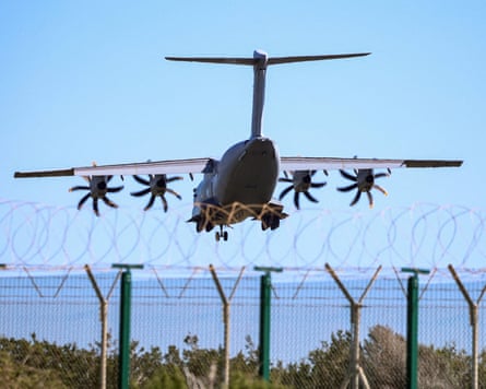 A large bomber plane in sky over a blue sea with a barbed wire fence in front