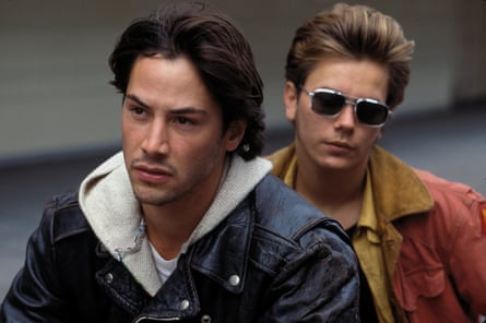 One dark haired boy and a blond boy wearing shades on the back of a motorbike