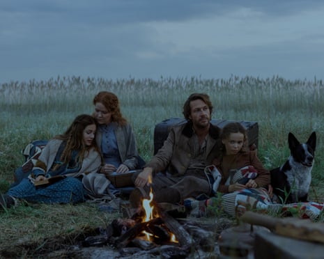 Family sits in grass around campfire in the evening