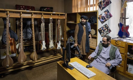 Two Taliban, one with an AK47, in an office with musical instruments lining the walls.