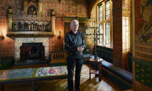 Jimmy Pages standing in the library of his home with its ornate fireplace and highly decorated walls
