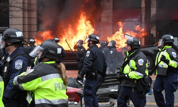Police officers move protesters away from a car that was set on fire during protests near the inauguration of Donald Trump in Washington.