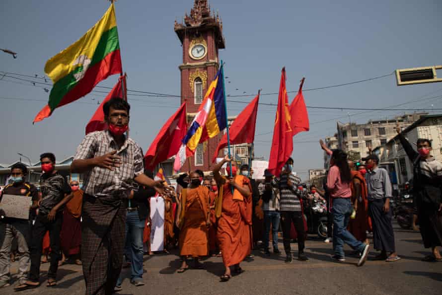 Monks in saffron-coloured robes with other protesters, many carrying flags, marching through a city