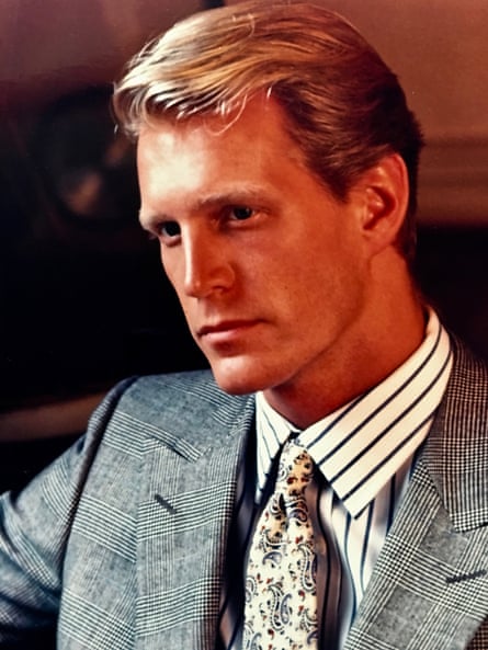 A man in a grey suit with a white/black striped shirt, a floral tie, and blond hair