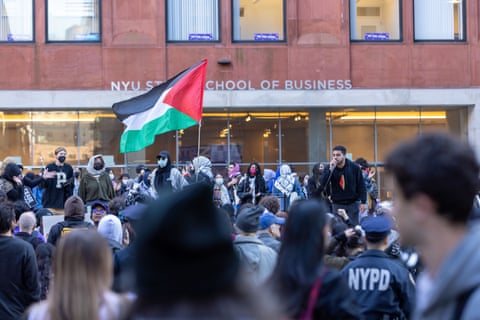 A person with a microphone addresses a crowd outside an NYU School of Business building