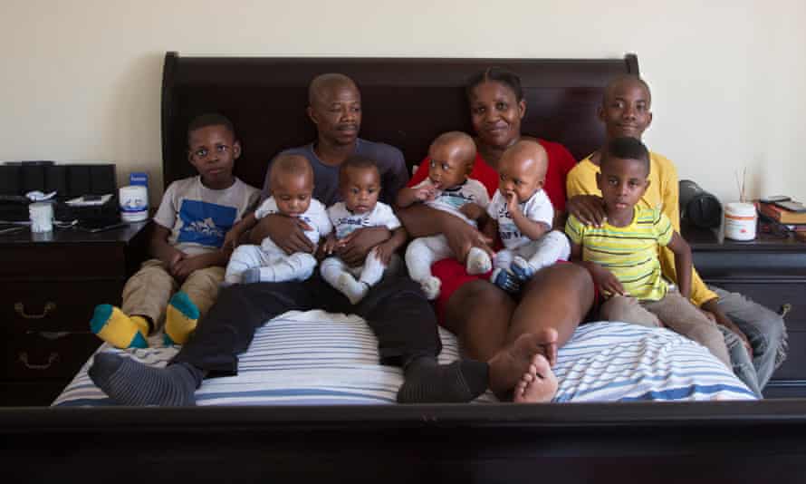 Keneilwe Ditsile and Otsile Kgafela hold their seven-month-old quadruplets on a bed with their three older sons.