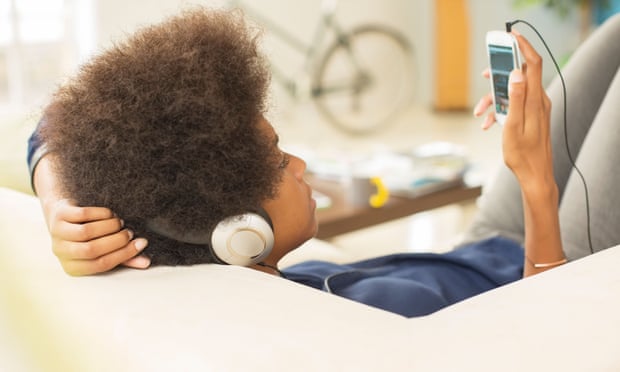 Someone listens through headphones on a sofa.