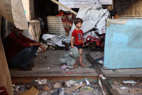 A child holds a stuffed animal while standing at a school sheltering displaced Palestinians which was hit by an Israeli strike in the Al-Bureij camp in the central Gaza Strip.