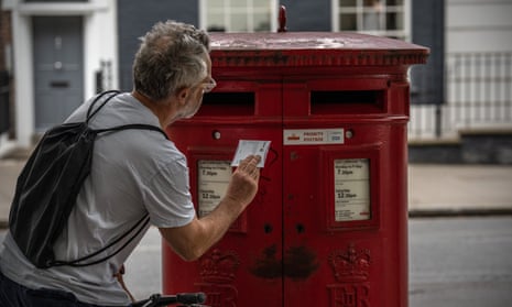 A man posts a letter in a Royal Mail postbox in 2022 in London, England. 