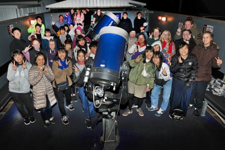 A group of people stand crowded around a large telescope at night