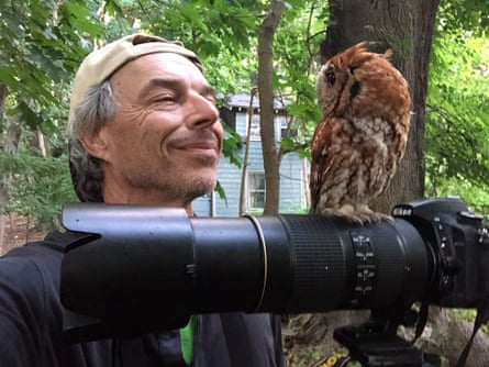 A man smiles at an owl, which is perched on the camera he is holding.
