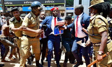 A young black man in a navy suit and red beret being bundled away by riot police