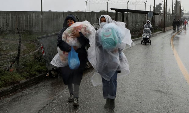 Two women carry their children during a rainfall, outside the Kara Tepe camp for refugees and migrants on the island of Lesbo
