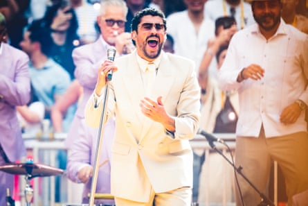Bad Bunny on stage in Madrid. He is wearing a pale cream suit, shirt and tie as he sings.